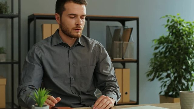 Portrait Of Tired Young Businessman Opening His Diary To Checking Plans For Tommorow While Drinking Coffe In The Office.