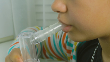 Girl breathing through a steam nebulizer. Treatment bronchopulmonary diseases. Teenager girl with...