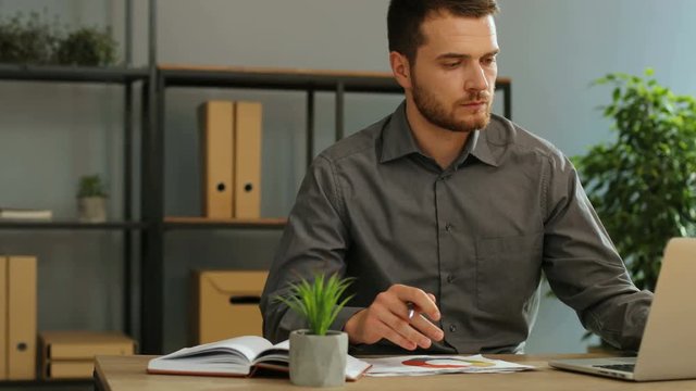 Handsome young business man working on laptop computer in the office and analizing the diagrams fron the finance report.