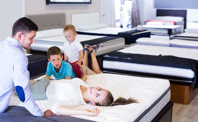 Cheerful woman with her family lying on back on mattress in store