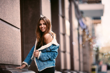 Outdoor portrait of a young beautiful fashionable happy lady posing on a street city. Model wearing stylish clothes. Girl looking up. Female fashion. City lifestyle. Copy space for text