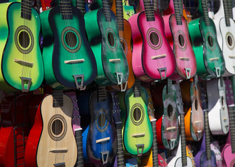 Naklejka premium Sunlit, Angular, Isolated View of Colorful Small Children's Toy Guitars Hanging Up