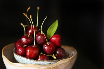 ripe fresh  cherry with leaves in a clay bowl on a dark background.Dark Key
