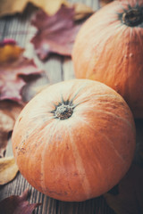 Pumpkins on  wooden table with fallen autumn maple leaves.