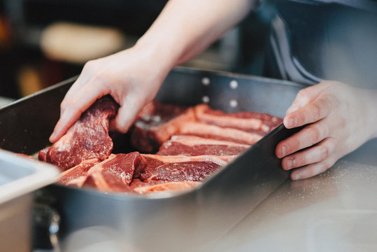 Chefs hand marinating steaks in an oven pan