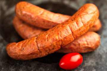 Pile of deliciously smoked handmade Swedish Isterband sausages with natural casing. Here with a tomato.