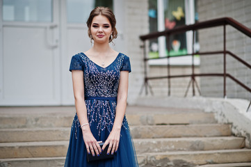 Portrait of an attractive girl standing and posing on the stairs in amazing gowns after high school graduation.