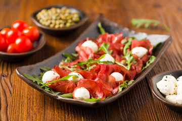 Beef carpaccio served with balls of mozzarella cheese, arugula and capers.