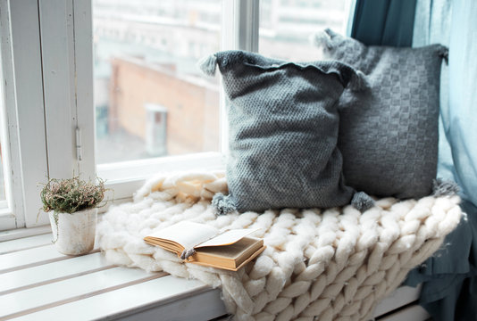 Warm and cozy window seat with cushions and a opened book, light through vintage shutters, rustic style home decor.