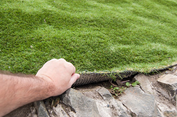 the hand of a man lifts an artificial grass cover