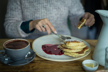 Girl eating pancakes with sort fruit marmelade and cappuccino for breakfast