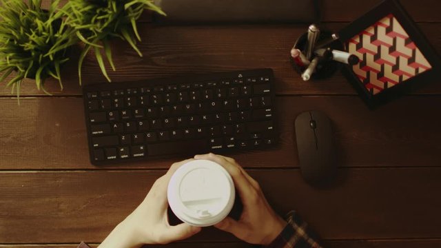Overhead shot of man with cup of coffee typing on keyboard