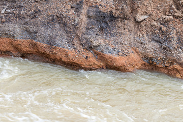 Water flows into gravel, rocks, under the road.