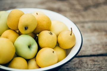 Fresh ripe yellow pears and apples in white bowl on natural wooden background. Selective focus