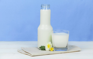 A bottle of milk and glass of milk on a wooden table on a  background