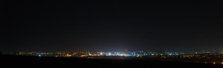 Fototapeta na wymiar The bright lights of the city streets in the background of the night sky. Panoramic view of residential areas.