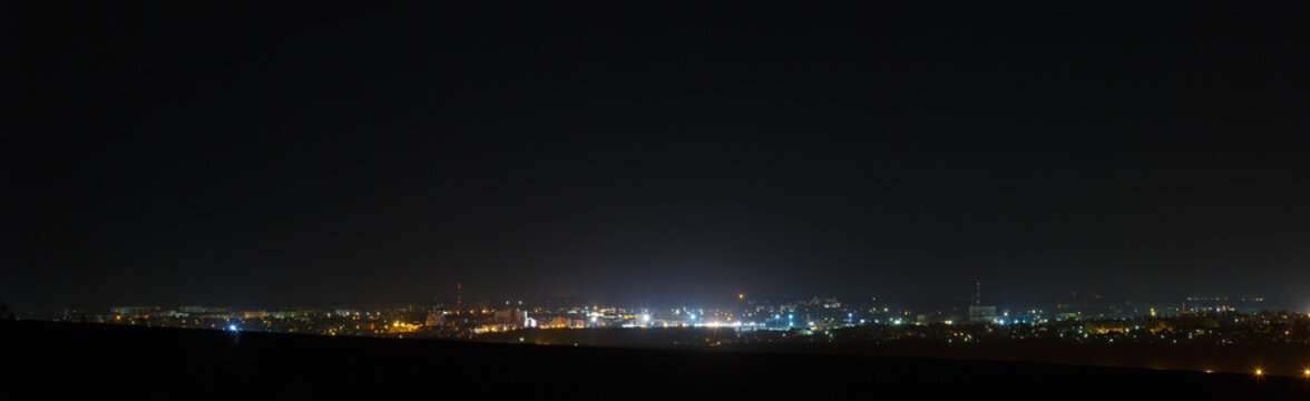 The bright lights of the city streets in the background of the night sky. Panoramic view of residential areas.