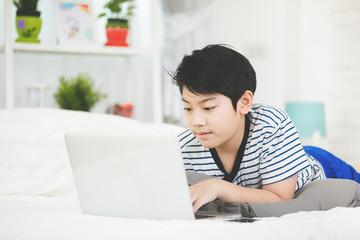 Cute asian boy rest on bed and typing laptop computer.