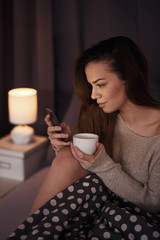 Girl drinking coffee and using smart phone in bed/ internet addiction concept