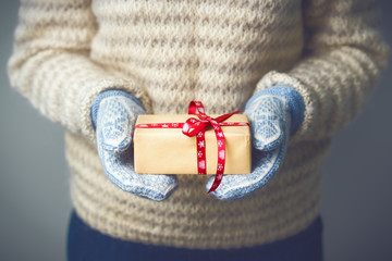 Christmas background. Girl in a warm knitted sweater and mittens is holding a Christmas present. Gifts for men. Merry Christmas. Gift for a girl. Knitted dress. Image is toned in fashionable color.