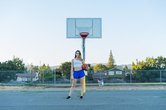 Casual sporty woman holding orange basketball on basketball street court