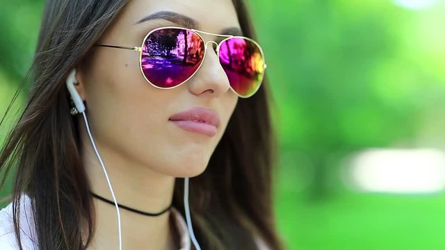Beautiful woman with glasses and earphones looks at the forward. Attractive girl in sunglasses with earpieces listens to music