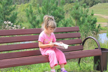 Девочка читает газету сидя на лавоке в парке возле реки. © tony775