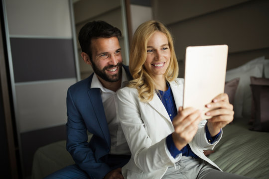 Businessman and businesswoman sitting on bed and using tablet