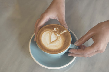 closeup hand holding coffee latte art cup on table.