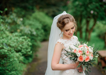 Fototapeta premium Beautiful blonde bride poses with orange wedding bouquet in the park