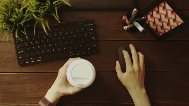 Overhead view of man using computer mouse with cup of coffee in other hand