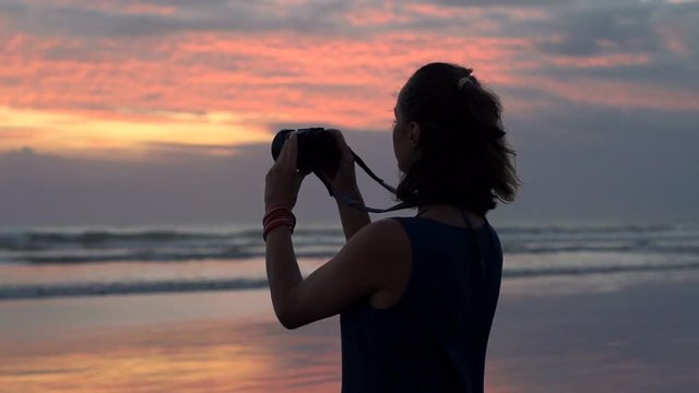 Woman taking photos of beautiful sunset with camera on beach, super slow motion 240fps
