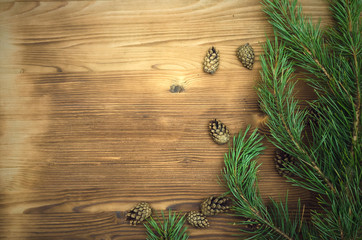 Fir tree branches with scattered cones around on brown wooden table surface background with copy space. Christmas table decoration.