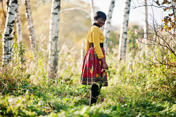 African american girl at yellow and red dress at golden autumn fall park.