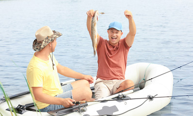 Two men with freshly caught fish in inflatable boat on riverside