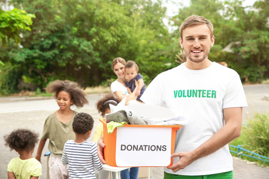 Young male volunteer holding box of donations outdoors
