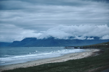 the austere Icelandic landscape with field in the foreground and the mountains and the fjords and the ocean in the background