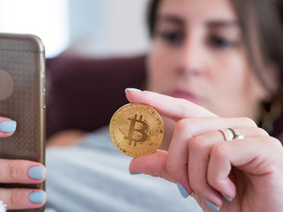 Young woman looking at smartphone and holding golden bitcoin