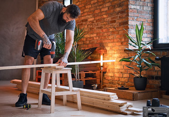 Carpenter drilling a hole in a board in a room with loft interior.