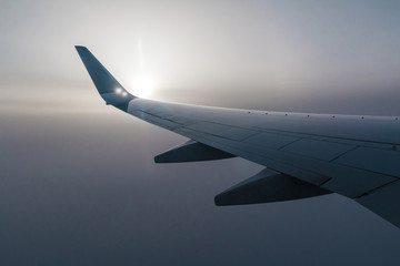 Naklejka premium Skrzydło samolotu i słońce przeświecające przez mgłę chmur.