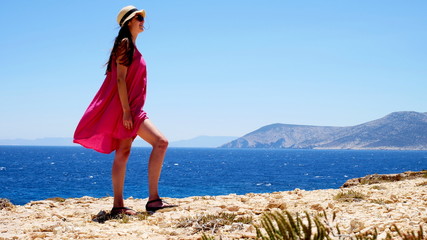 Europe's Secret Islands/ Woman in pink dress staying on a mountain looking to the right with sea in background.