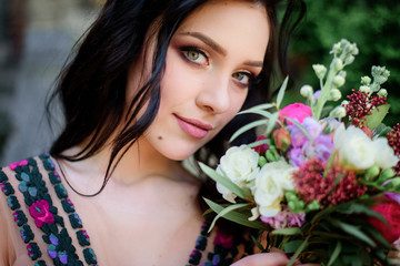 Naklejka premium Stunning brunette woman in dress with flowers stands in the garden