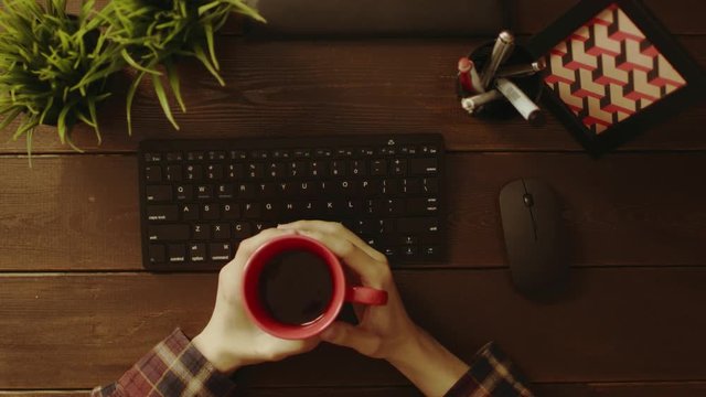 Overhead shot of man drinking coffee while sitting in front of computer