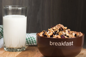Homemade granola with honey, oatmeal, cashew nut, almond, pistachio, raisin and cranberry in clay bowl,glass with milk on wood dark table,