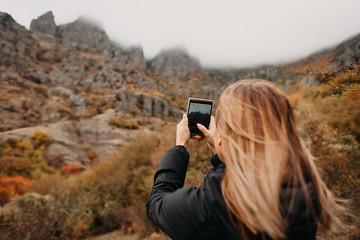 A young girl takes photos of a autumn mountain landscape. Foggy day