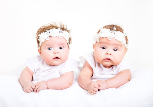 Two cute kids lying on the white background. Portrait of twins in white gowns and bandages on their heads on a white background