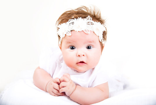 cute kid lying on the white background. Portrait of baby in white gown and bandage on her head on a white background