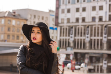 Fashion portrait of young glamorous woman wears wide-brimmed hat. Lady posing on a background of city