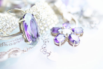 Beautiful elegant luxury composition of from silver and platinum jewelry with ring,  flower pendant and big amethyst gemstone and diamonds on light silvery background close-up macro. Selective focus.