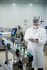 Young employee in professional uniform working on production machine of cosmetics.